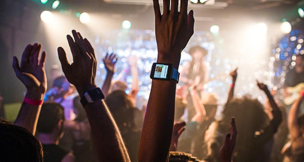 Image of a concert attendee holding up their arms, with an Android Wear watch visible.