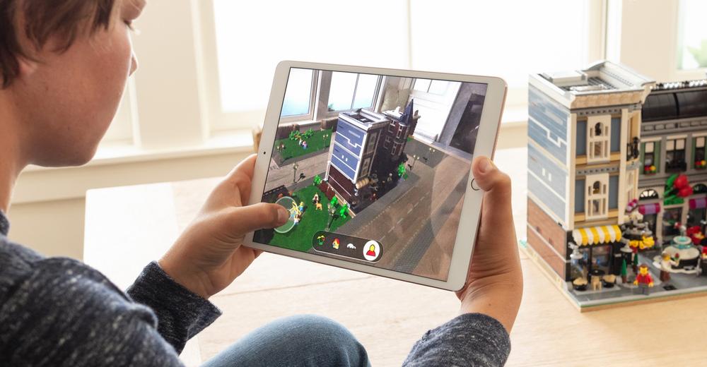 Photograph of a child playing with augmented reality features on an iPad, showing Lego characters on the screen as he points the camera to a Lego city in the real world.
