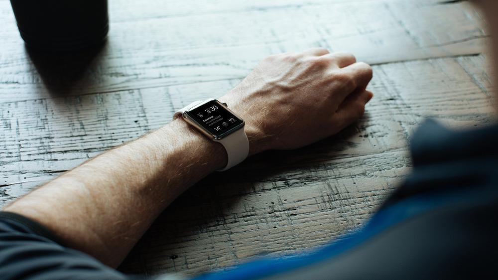 Image of a person's arm wearing an Apple Watch, resting on a table.