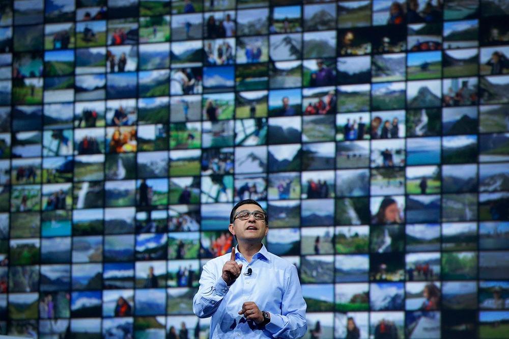 Image of Google executive Vic Gundotra introducing new Google+ photos features on stage, flanked by a large grid of photographs.