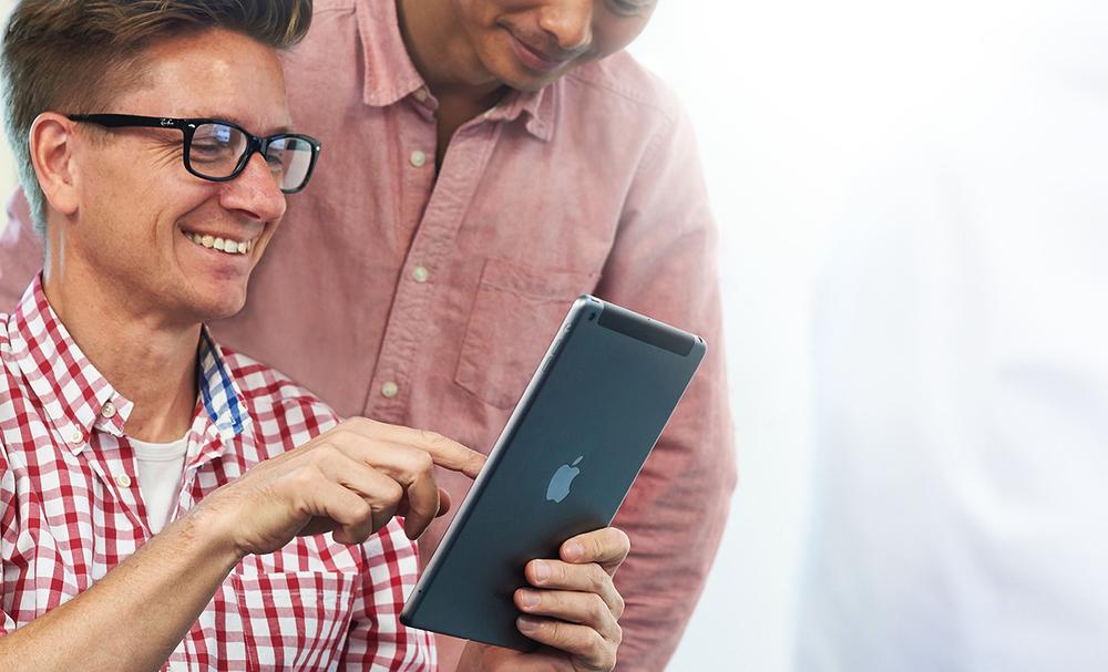 A man smiles while showing another man something on an iPad, presumably a delightful incentive-based design pattern.