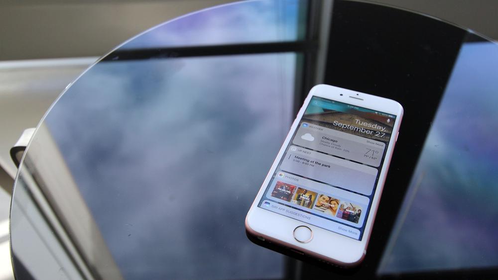 A picture of an iPhone on a table next to the window of a skyscraper, overlooking Millennium Park in downtown Chicago, with iOS 10 Notification Center widgets shown on its screen.