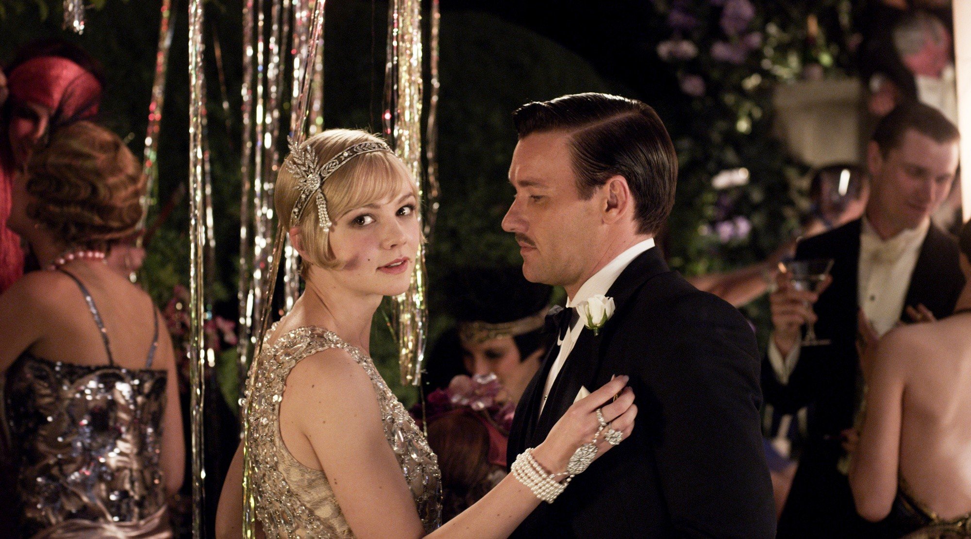 A still from the 2013 live-action adaptation of *The Great Gatsby*, where Daisy Buchanan, played by Carey Mulligan, looks to the camera as she dances with her husband.